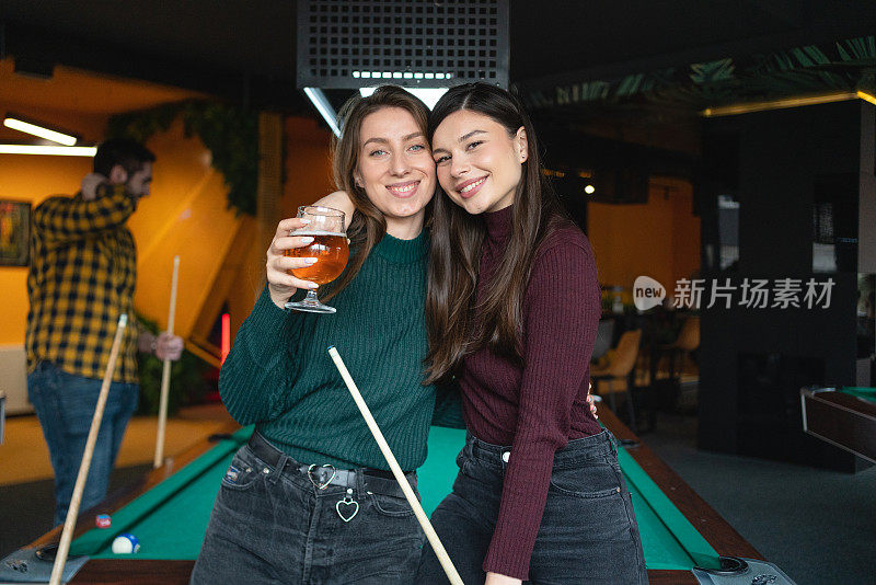 照片上的女性朋友抱着啤酒，一边打台球桌