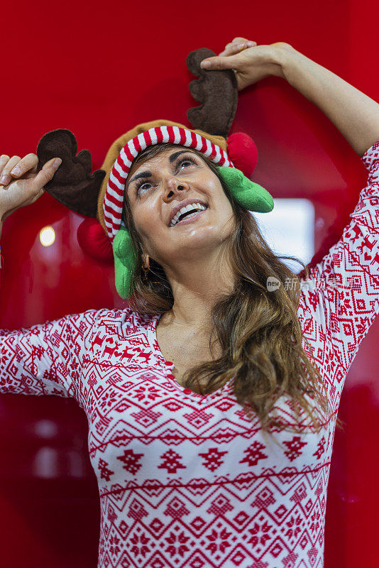 平均年龄40岁的拉丁裔妇女站在红色背景墙上，穿着圣诞睡衣和驯鹿帽