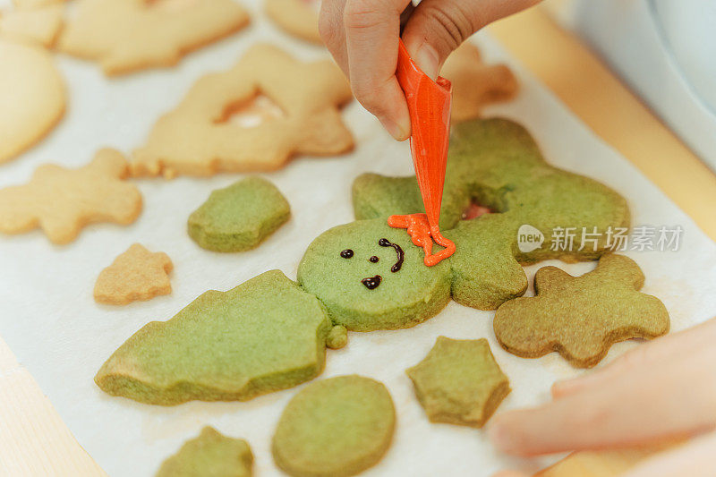 近距离的手装饰姜饼人圣诞饼干与绘画和巧克力在烤盘上