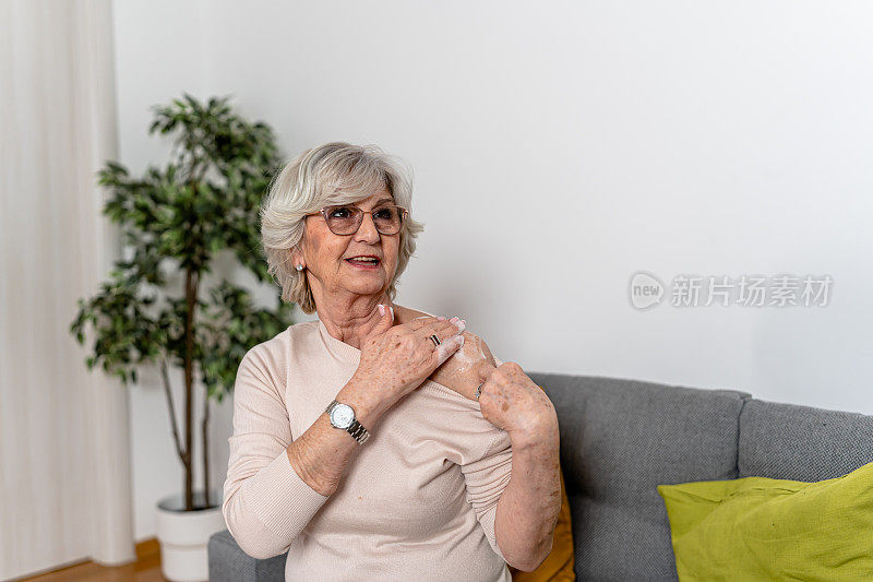 在接受激素替代治疗时，一名头发花白的妇女正在肩膀上涂药膏。