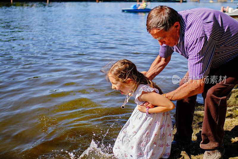 小女孩在爷爷的搀扶下在河里泡脚