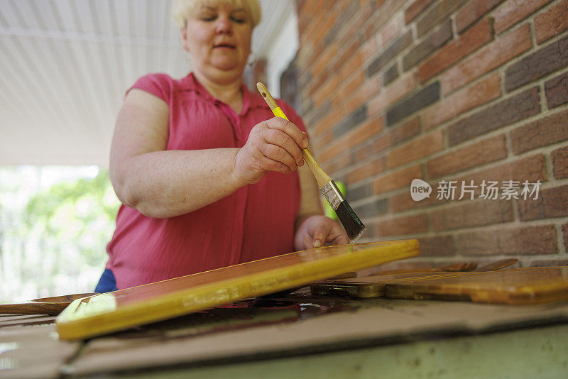 用油漆刷在硬木上涂矿物油。成熟的金发女人用矿物油刷保护和保养木制砧板。用刷子把重点放在手上