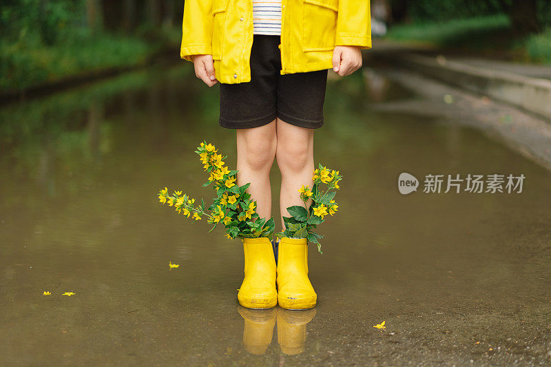 春天的一天，可爱的小男孩穿着雨衣和胶靴走过水坑