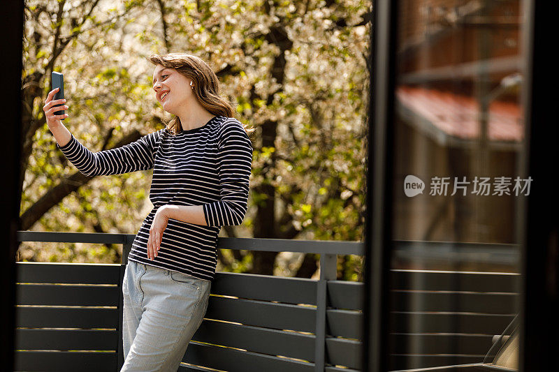 年轻女子在阳台上放松，和朋友视频聊天