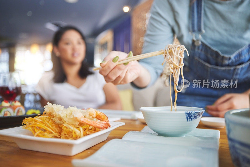 手、拉面和筷子为中餐与一位女士近距离在餐厅用餐。和顾客一起在餐馆里吃汤、面条和美食，以补充营养或享用传统的日本晚餐