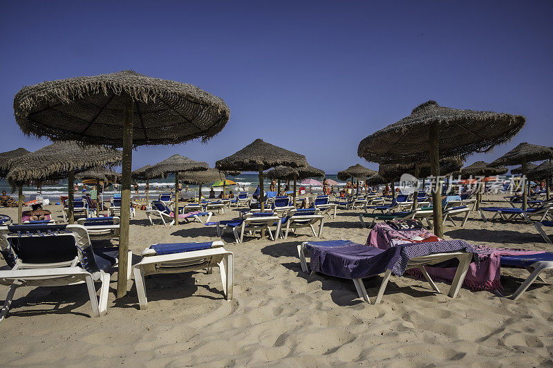 夏天的西班牙海滩，沙滩上有一排排的躺椅和遮阳棚