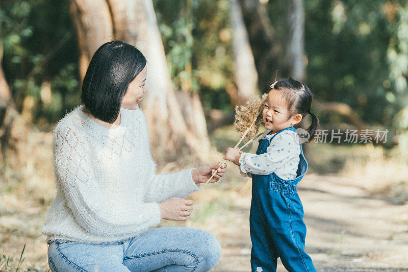 一位母亲和她的女儿站在对方面前，手里拿着干花。