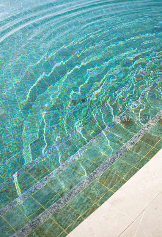 游泳池边缘与绿松石瓷砖和水面上的阳光