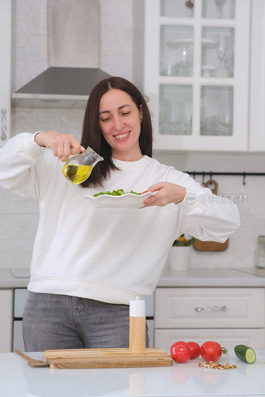 厨房里的女厨师正在准备蔬菜沙拉。健康饮食。饮食的概念。健康的生活方式。在家做饭。做饭。这个女人正在把油倒在沙拉上。
