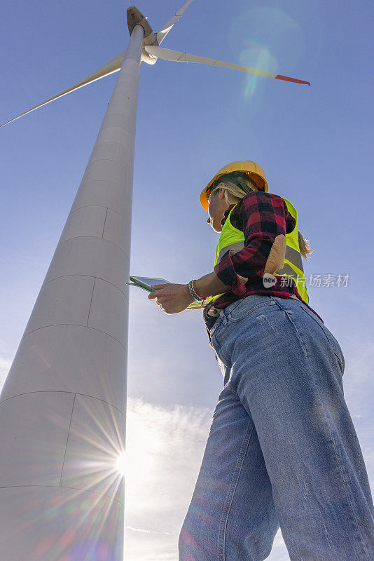 一名女工程师正在检查用于可再生能源生产的风力涡轮机基础设施，她正在使用数字平板电脑记录现场数据