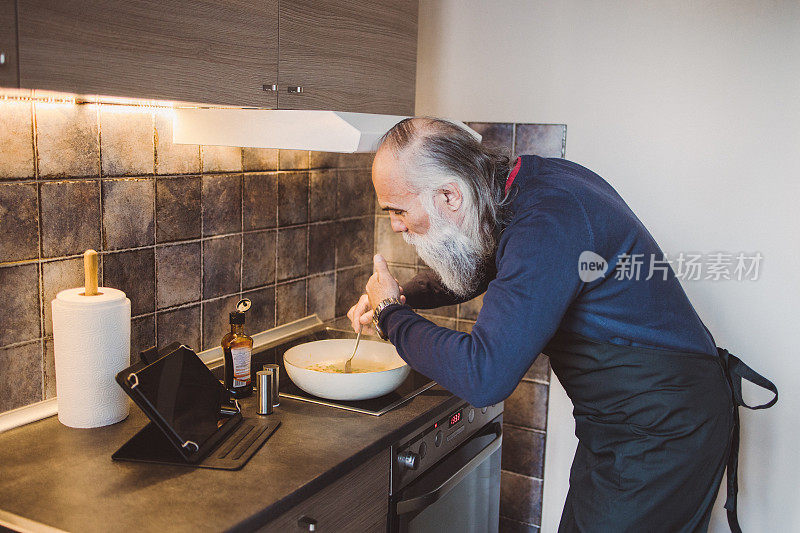 一名留着长胡子的成年男子通过数字平板电脑观看烹饪教程