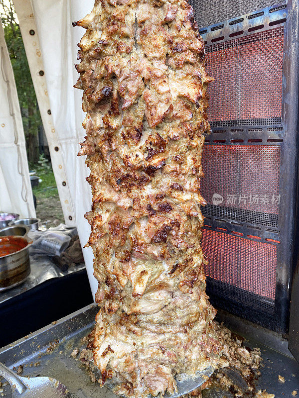 土耳其风格的doner烤肉串在金属格栅上的特写图像，肉在垂直旋转的烤炉上烹饪，鸡肉堆叠在倒锥形的形状
