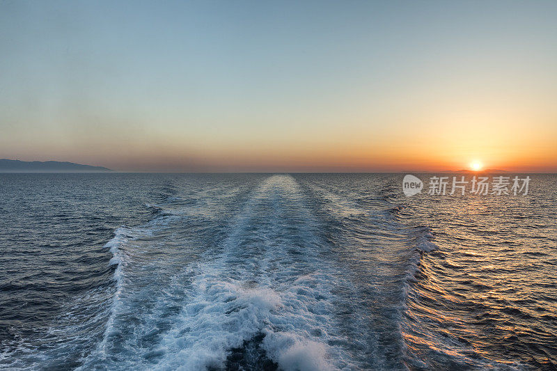 在穿越希腊基克拉迪斯群岛的渡轮后面的日落