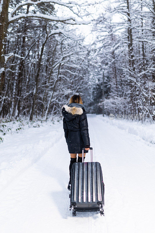 亚洲女性旅行与行李箱下雪林路