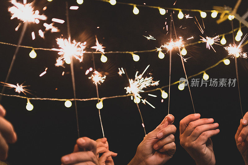 一组四人享受新年之夜，中间放着烟火，看着镜头——成年人在一起玩得很开心