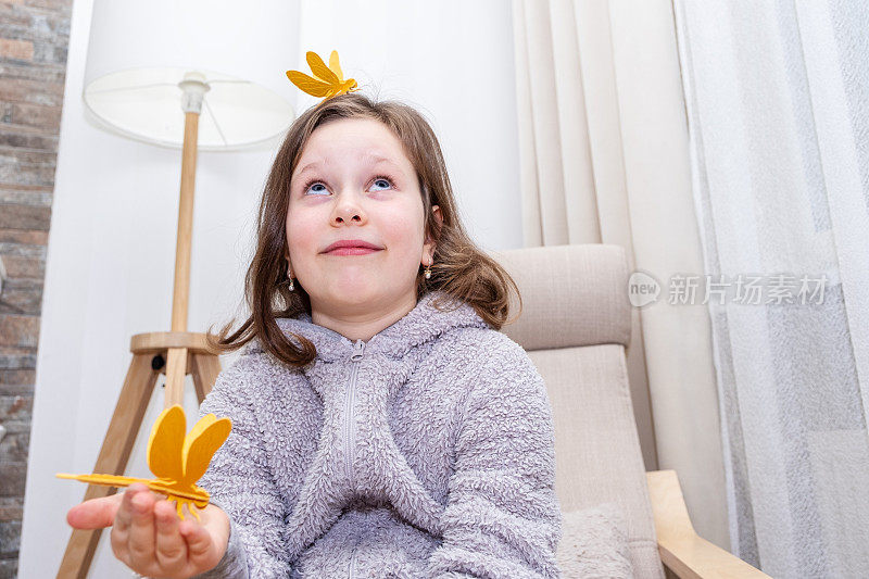 一个7岁的白人女孩，用木制玩具组装了一只蜻蜓，开心地笑着，一只蜻蜓坐在她的头上。