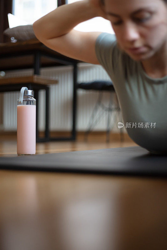 年轻女子在家里的客厅锻炼期间补水。