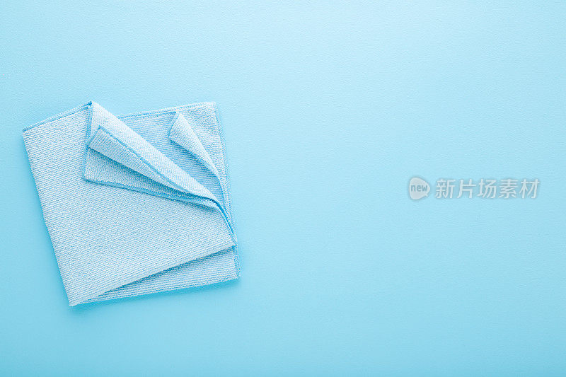 可折叠的干软超细纤维抹布，适用于不同表面，在浅蓝色的桌面背景上擦拭。柔和的颜色。特写镜头。文本的空白位置。自顶向下视图。