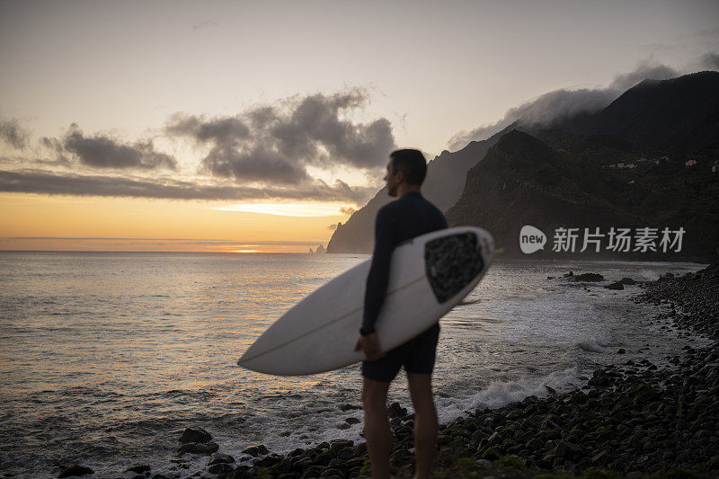 拂晓时分，冲浪者带着冲浪板眺望大海。