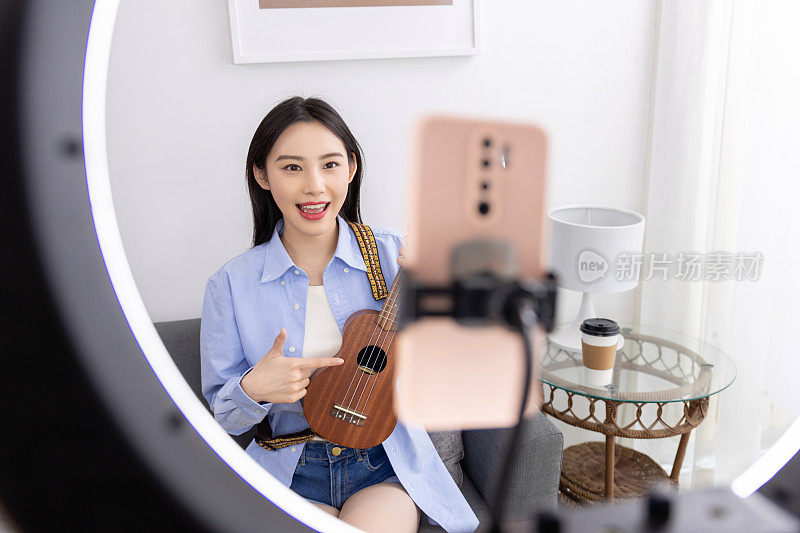 年轻女子在家里用笔记本电脑学习在线尤克里里吉他课程。学习一种乐器。