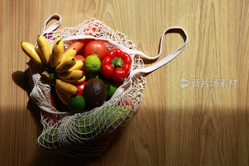 一个环保的可重复使用的购物袋，装满了五颜六色的新鲜蔬菜和杂货，放在家里的桌子上，代表了零浪费和可持续生活方式的概念