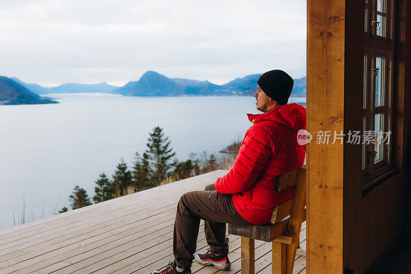 一名男子在挪威的山上俯瞰风景优美的峡湾，沉思冬日