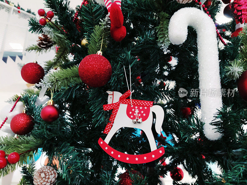 圣诞树上有装饰品、圣诞球和玩具。红白挂饰。美丽的球，明亮的浆果和球果。雪糖棒。玩具-摇马