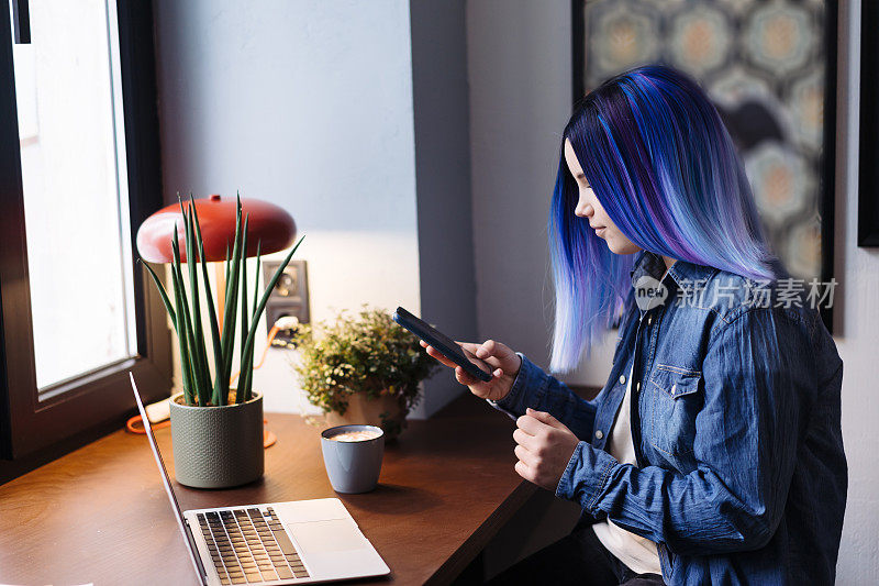 迷人的年轻拉丁裔女孩的肖像，蓝头发，蓝色牛仔衬衫，坐在咖啡馆里使用智能手机，有复制空间。