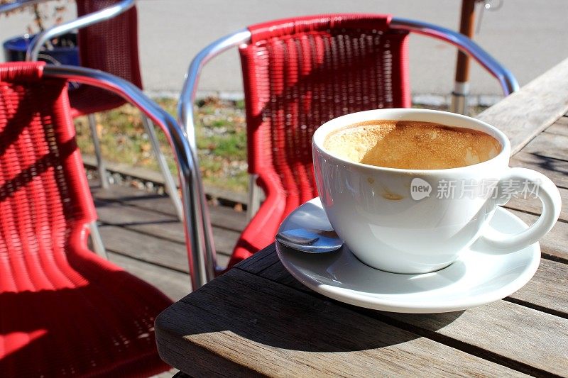 一杯卡布奇诺，背景是一把红椅子。咖啡厅阳光明媚的露台上的一张桌子。