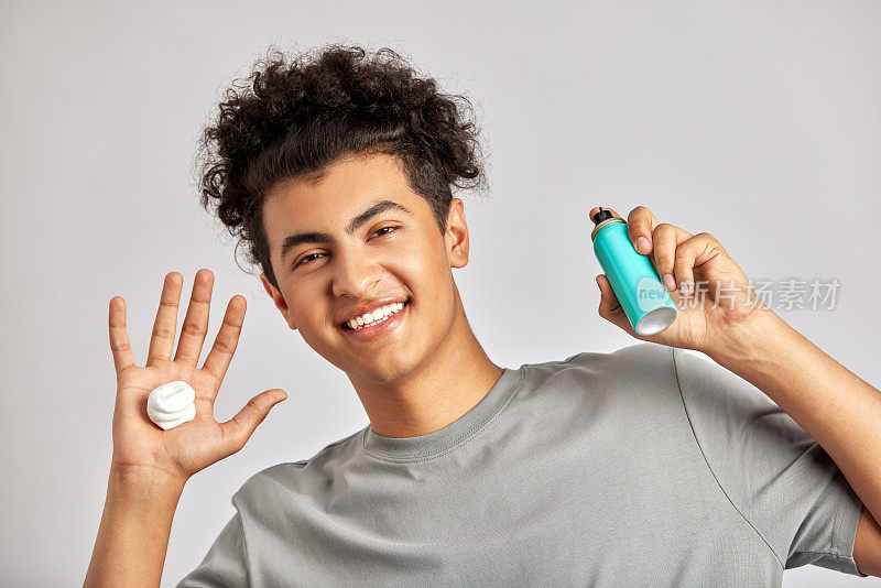 黑色卷发的年轻人将洗面奶涂在手上，准备开始他的日常美容和护肤程序。男士准备好好洗脸，为肌肤清新健康打下基础。