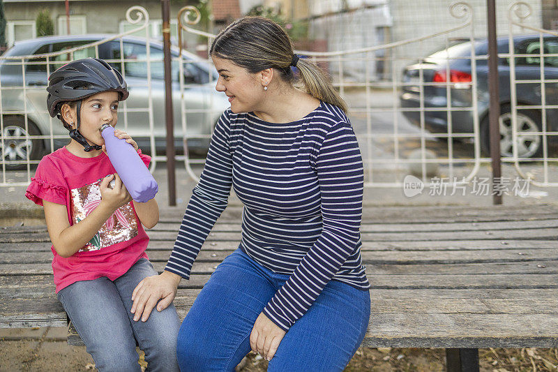 一个小女孩和妈妈坐在长凳上喝水