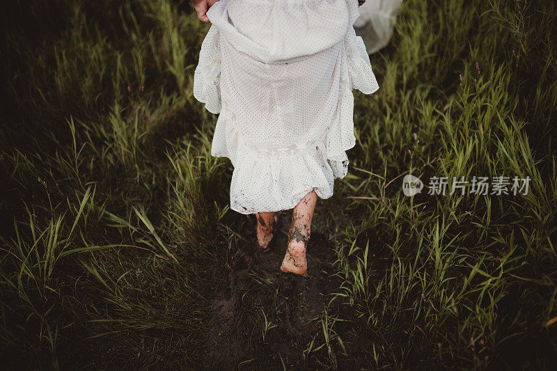 年轻的女孩光着脚，穿着长裙，在泥泞中奔跑