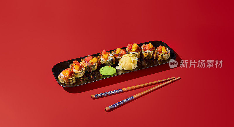 配有浓郁柑橘酱的天妇罗寿司卷，装在黑色盘子里。现代静物在深红色的背景与硬阴影。亚洲餐厅的理想旗帜