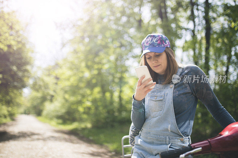 漂亮的年轻女子戴着帽子坐在摩托车上用智能手机。