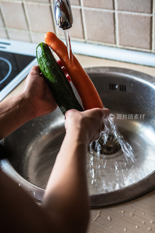 一个女人在厨房水槽里洗蔬菜的特写。