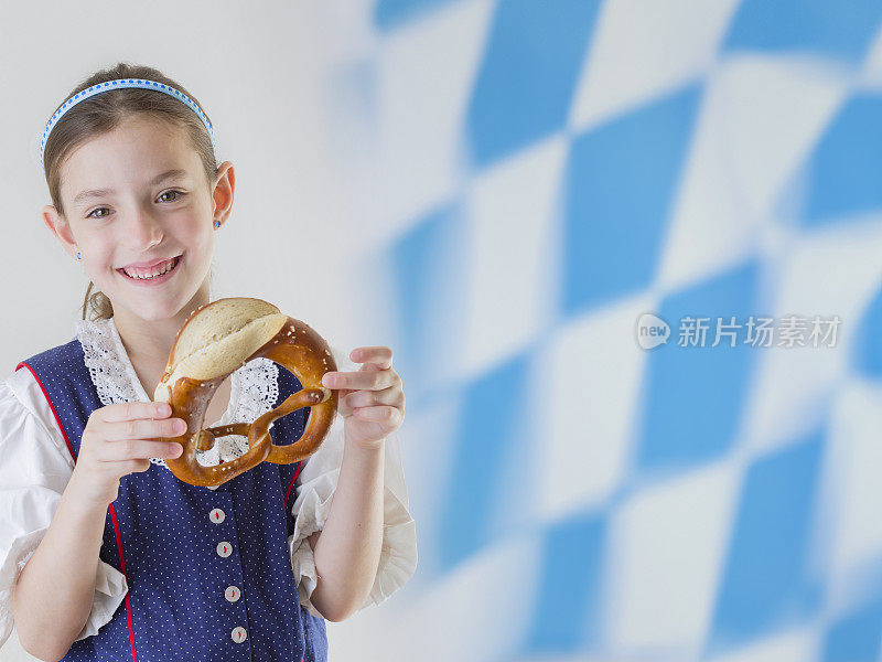 巴伐利亚小女孩穿着传统连衣裙，腰裙和椒盐卷饼巴伐利亚旗