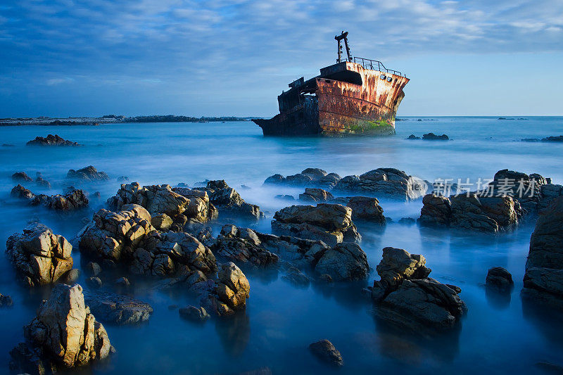日落时，一艘老船的残骸长时间暴露在岩石上