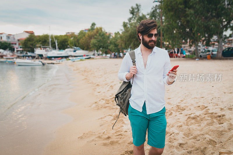 一个背着背包的男人在海滩上用手机