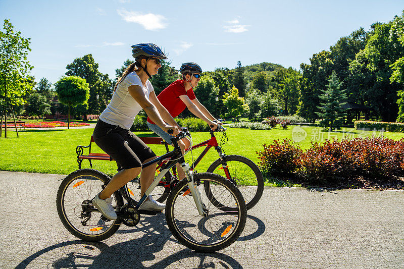 城市自行车-女人和男人在城市公园骑自行车