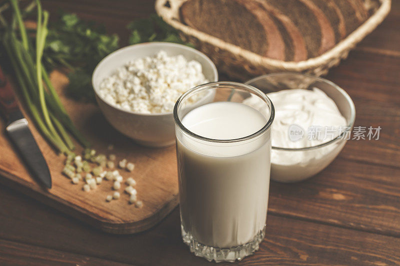 一杯牛奶，碗里的凝乳，芝士奶油，新鲜培育和绿色的草本植物在木砧板上作为自制健康饮食素食的原料