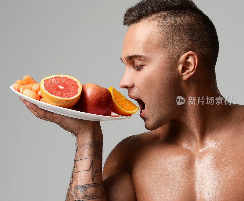 年轻、强壮、肌肉发达的运动员吃新鲜的素食、胡萝卜、橙子、葡萄柚和苹果。