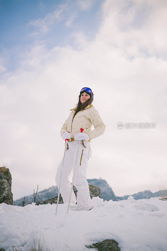 近景美丽的年轻女子在冬天的衣服站在一边，手拿木棍的背景雪山