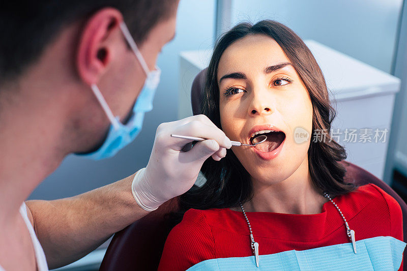 很酷的工作,医生!一个穿着红毛衣的漂亮女孩去看牙医。牙医正在用牙齿检查镜检查他的工作结果。