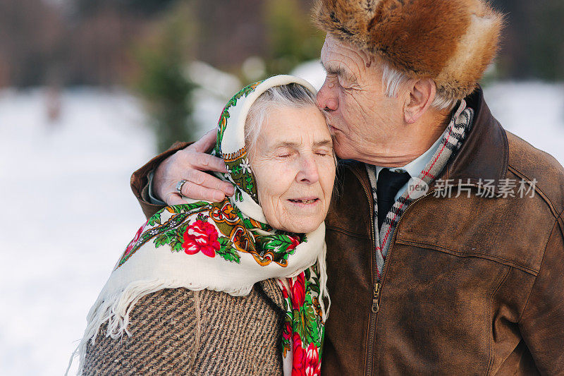 老年夫妇的肖像。老人亲吻他的妻子在重量。冬天的时候，一对老夫妇在公园里散步。幸福的家庭。金婚