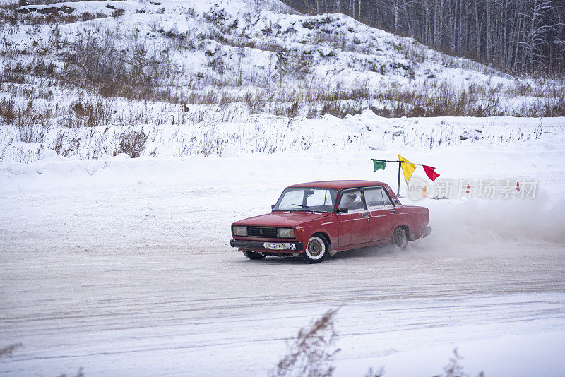 俄罗斯旧的低红色汽车“瓦兹-日古力”在转弯漂移旋转车轮升起雪走得很快。
