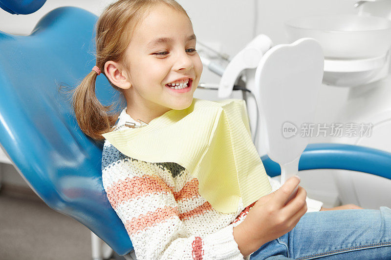 看完牙医后，小白种女孩对着镜子微笑。