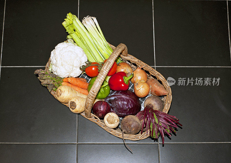 在黑色瓷砖地板上的柳条篮子里五颜六色的新鲜蔬菜