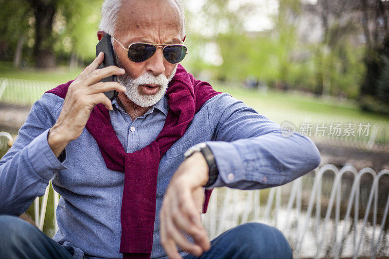 一个老人正在室外一边看他的手表一边讲电话