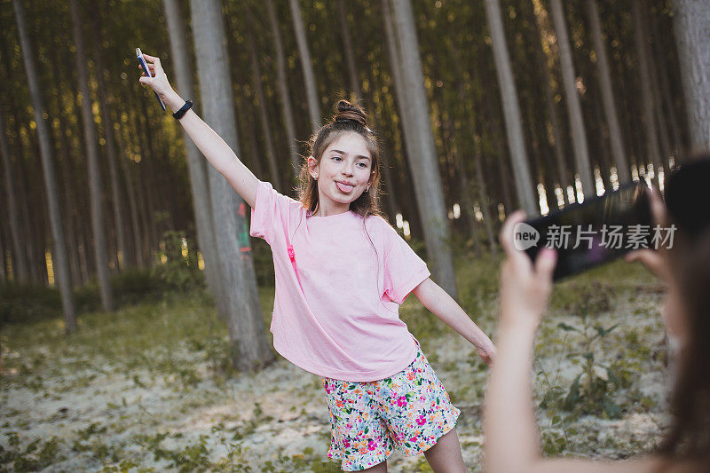 快乐的女孩在森林里用手机拍照。