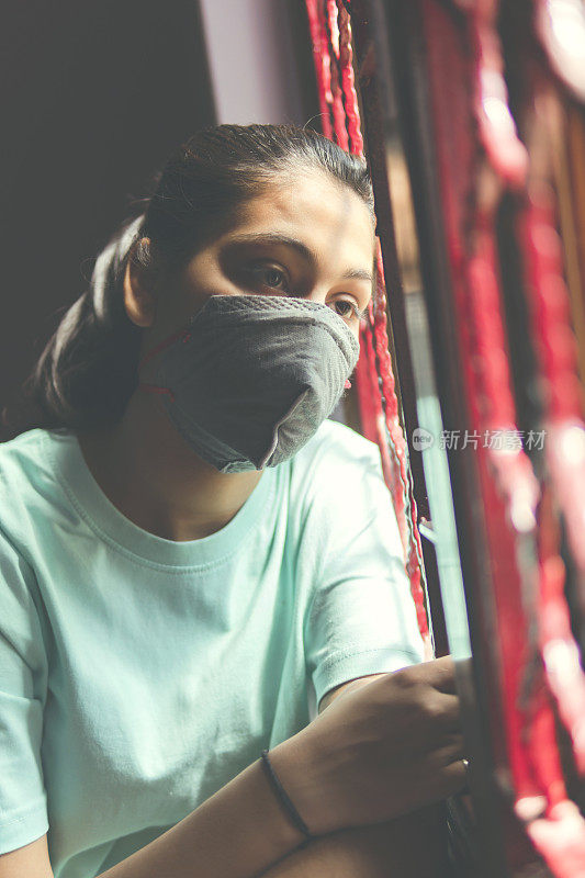 这个悲伤的女孩正在保护自己，戴着口罩，在家里自我隔离。